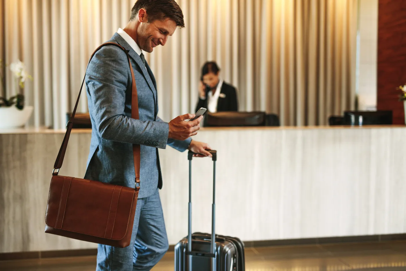 Guest with a suitcase looking at their phone in front of a hotel reception desk