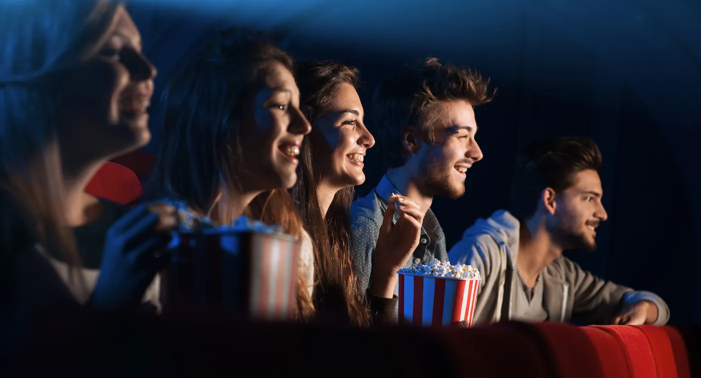 Grupo de amigos riendo en las butacas de un cine con palomitas